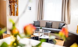 An inviting living room with a gray sofa and a glass table. In the foreground, there are flowers that give the room a fresh atmosphere.