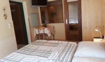 A cozy bedroom with a large bed and wooden paneling. There is a table and chairs as well as a television on the wall.