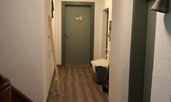 A bright hallway with gray walls and wooden flooring. At the end of the hallway, there are several doors.