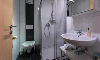 A modern bathroom with a shower and a sink. The walls are light tiled, and there are elegant fixtures.