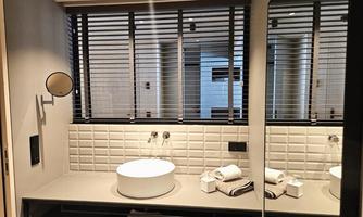 A modern bathroom with an elegant sink and a large mirror. The blinds provide pleasant lighting and privacy.