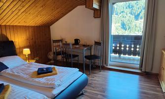 A cozy bedroom with two single beds and wooden walls. There is a table with chairs and a balcony overlooking the mountains.