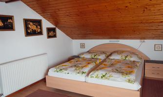 A cozy bedroom with a double bed and wooden ceiling. Pictures hang on the walls, and there is a modern radiator.