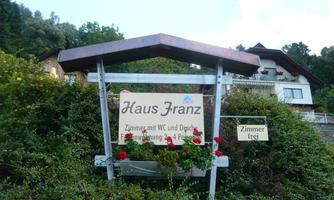 A sign with the inscription "Haus Franz" stands in front of a flower box. It displays information about rooms with a toilet and shower for four people.