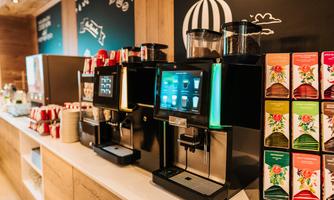 A modern coffee bar with multiple coffee machines and a selection of teas. The environment is brightly and invitingly designed.