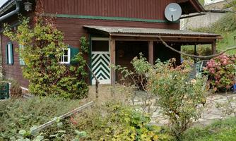A charming red wooden house with a covered entrance. Surrounded by green plants and colorful flowers.