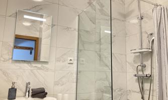 A modern bathroom with a glass shower cabin and marbled walls. A few towels and a bar of soap are on the sink.