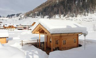 A cozy wooden house in the snow, surrounded by a winter landscape. Gentle hills and snow-covered roofs characterize the idyllic scene.