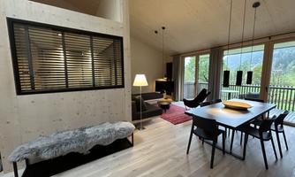 A modern living room with wooden interior and large windows. The room is bright and inviting, featuring a dining table and a cozy seating area.