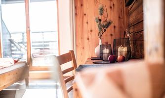 A cozy room with wooden paneling and a window. On the table are decorative elements like a vase, candles, and fruits.