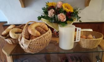 A beautiful breakfast table with fresh rolls in baskets and a pot of milk. There is also a bouquet of colorful flowers.