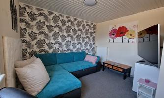 A cozy living room with a turquoise sofa and decorative cushions. Stylish flower artworks and a modern TV unit can be seen on the wall.