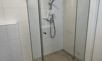 A modern shower with glass walls and a convenient showerhead. The floor is in neutral tones.