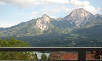 An impressive mountain landscape with high peaks and green hills. In the foreground, a cozy balcony can be seen.