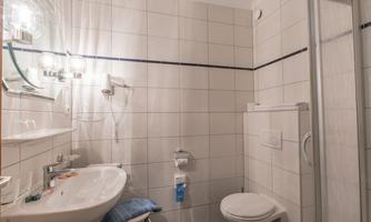 A modern bathroom with white tiles, a sink, and a shower. There is also a toilet and a mirror with lighting.