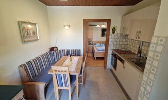 A cozy kitchen with a dining table and a seating area. In the background, another room is visible.