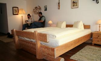 A cozy bedroom with a large wooden bed and soft lighting. Two people are sitting relaxed in the room and enjoying the atmosphere.