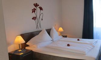 A cozy bedroom with a double bed and fresh bedding. Stylized flowers are depicted on the wall, and there are warm light sources.