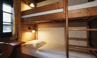 A cozy room with a wooden bunk bed. The walls are light, and there is a window with curtains.