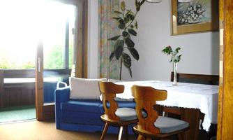A cozy dining area with a wooden table and two chairs. A blue armchair and a plant create a pleasant atmosphere.
