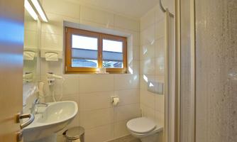 A modern bathroom with a shower, sink, and toilet. Large windows provide bright light.