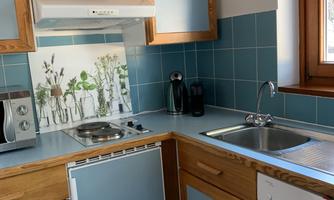 A cozy kitchen with wood-colored cabinets and blue tiles. It is bright and well-equipped with appliances.