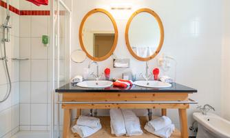 A modern bathroom with two sinks and round mirrors. The shower is adjacent, and fresh towels are ready.