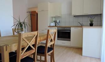 A modern kitchen with light wood and white furniture. A dining table with chairs is located in a cozy room.