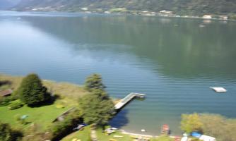 A tranquil lake landscape with gentle hills in the background. In the foreground, green meadows and a wooden pathway can be seen.