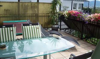 A cozy terrace with a glass table and lounge chairs. Colorful flowers and a green plant create an inviting atmosphere.