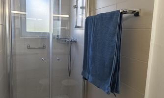 A modern bathroom with a glass shower cubicle. Hanging towels and a stool complement the space.