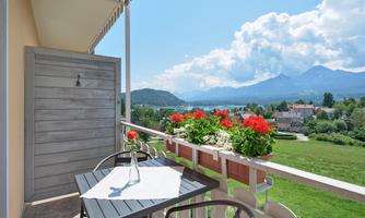 A beautiful balcony with a table and chairs, surrounded by blooming flowers. In the background, mountains and a clear sky are visible.