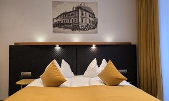 A modern bedroom with a large bed and yellow cushions. A historical photo of a building hangs on the wall.