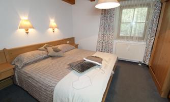 A cozy bedroom with a double bed and soft lamps. Large windows let in plenty of daylight, creating an inviting atmosphere.