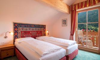 A cozy room with two single beds and a wooden ceiling. The window offers a beautiful view of the mountains and the balcony.