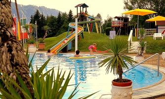 A swimming pool with a slide and playing children. In the background, there are palm trees and beautiful landscapes.