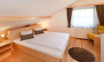 A modern bedroom with two beds and wooden furniture. The room is bright and inviting, with a window and a cozy armchair.