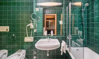 A modern bathroom with green tiles and a sink. There is a shower and a mirror that reflects the space.