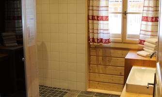 A bright bathroom with wood paneling and windows in classic design. The floor is made of stone tiles and there is a modern washbasin.