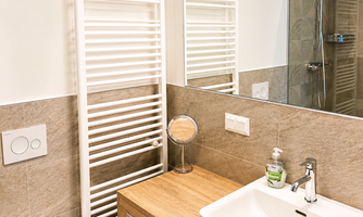 A modern bathroom with a white radiator and a wooden sink. The walls are bright and the mirror reflects the room.