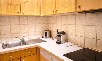 A modern kitchen with wooden shelves and a bright countertop. On the countertop, there is a faucet, a coffee machine, and an induction stove.