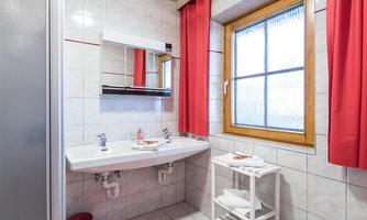 A modern bathroom with white tiles and red curtains. A sink and a mirror are clearly visible, as well as a window with natural light.