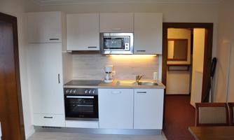 A modern kitchen with white cabinets and a work surface. It is equipped with a stove, a microwave, and a coffee maker.