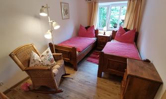 A cozy room with two single beds and pink pillows. Next to the beds is a chair and a nightstand.