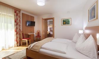 A cozy bedroom with a double bed and white pillows. The surroundings are bright and friendly, with a small table and chairs as well as a television.