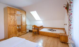 A cozy bedroom with wooden furniture, a large wardrobe, and a window. There is a bed and a small table with chairs.