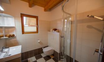 A modern bathroom with a shower, a sink, and a toilet. The walls are tiled in light colors, and there are wooden details on the ceiling.