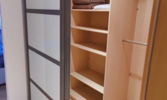 A modern cabinet with glass doors and open shelves. The inside is bright and well organized with towels.