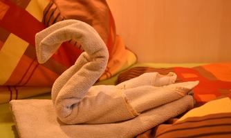 An artistically folded towel in the shape of a swan. It is placed on a bed with colorful pillows.