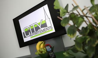 A screen with the logo "CITY Appartements" stands on a table. In the foreground, fresh fruits and a plant can be seen.